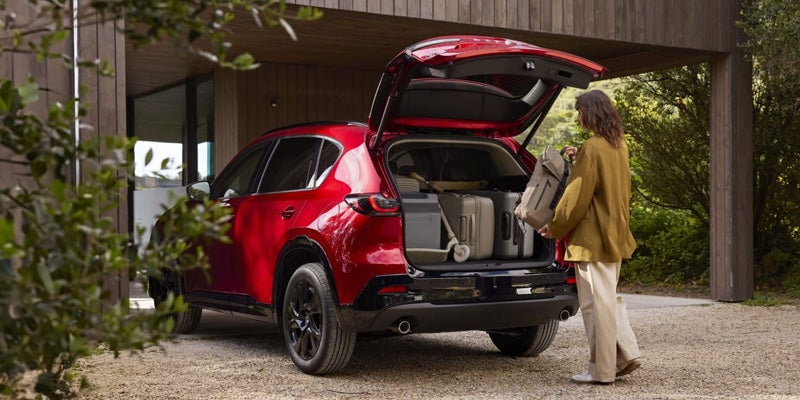 Person loading luggage into the rear cargo area of a red Mazda CX-5 parked outside a modern house.