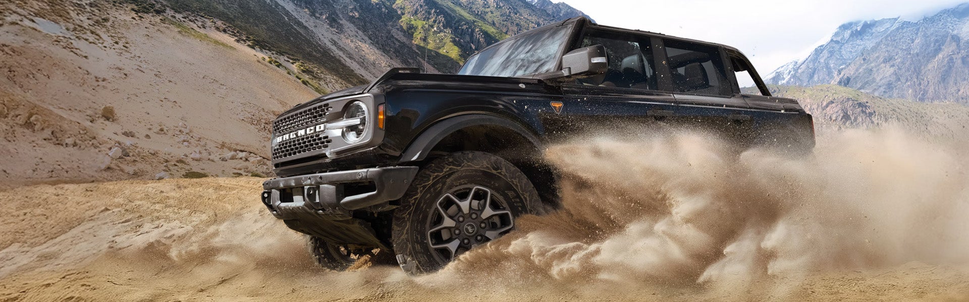 Black Ford Bronco SUV kicking up sand on a desert dune.
