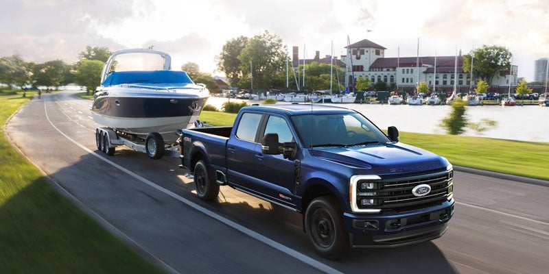 Blue Ford Super Duty towing a large boat near a marina