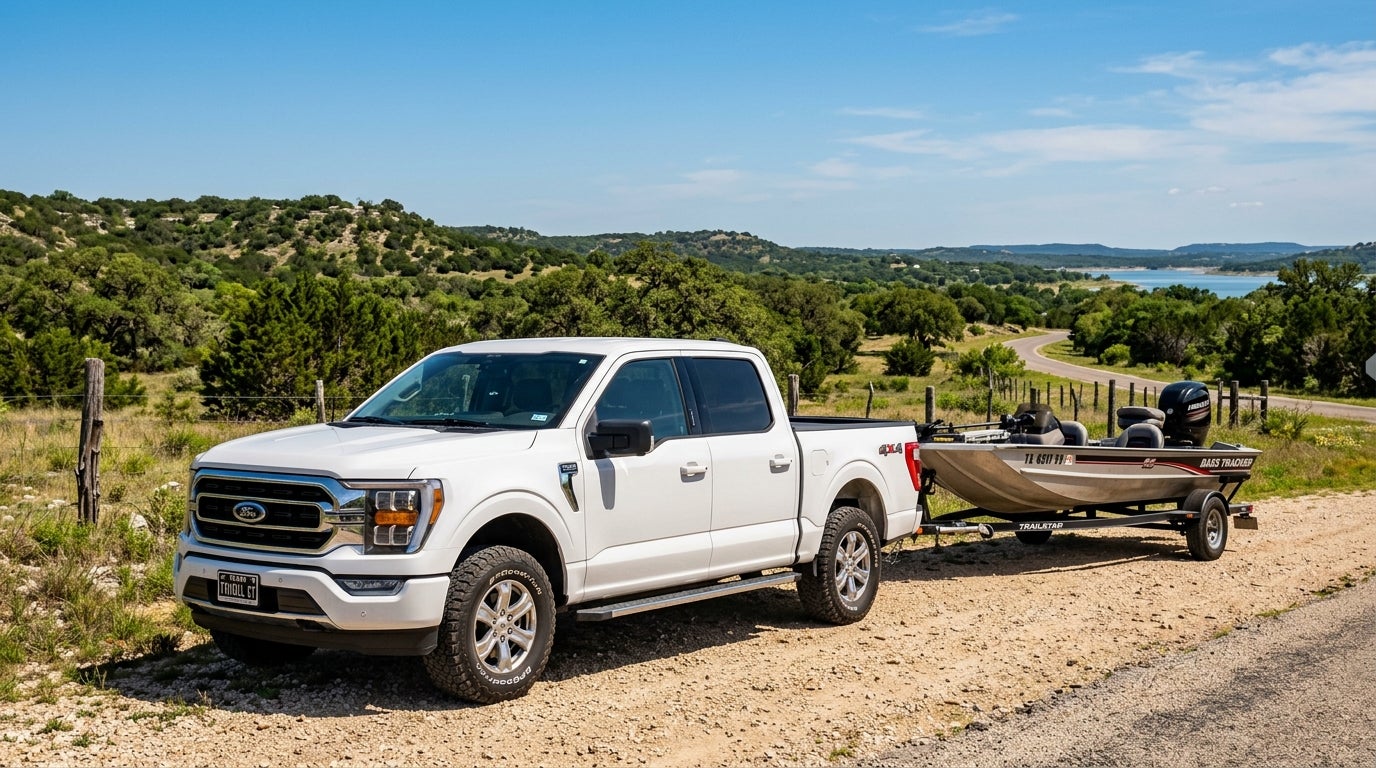A white Ford F-150 truck towing a Bass Tracker fishing boat on a dirt road overlooking a scenic valley.