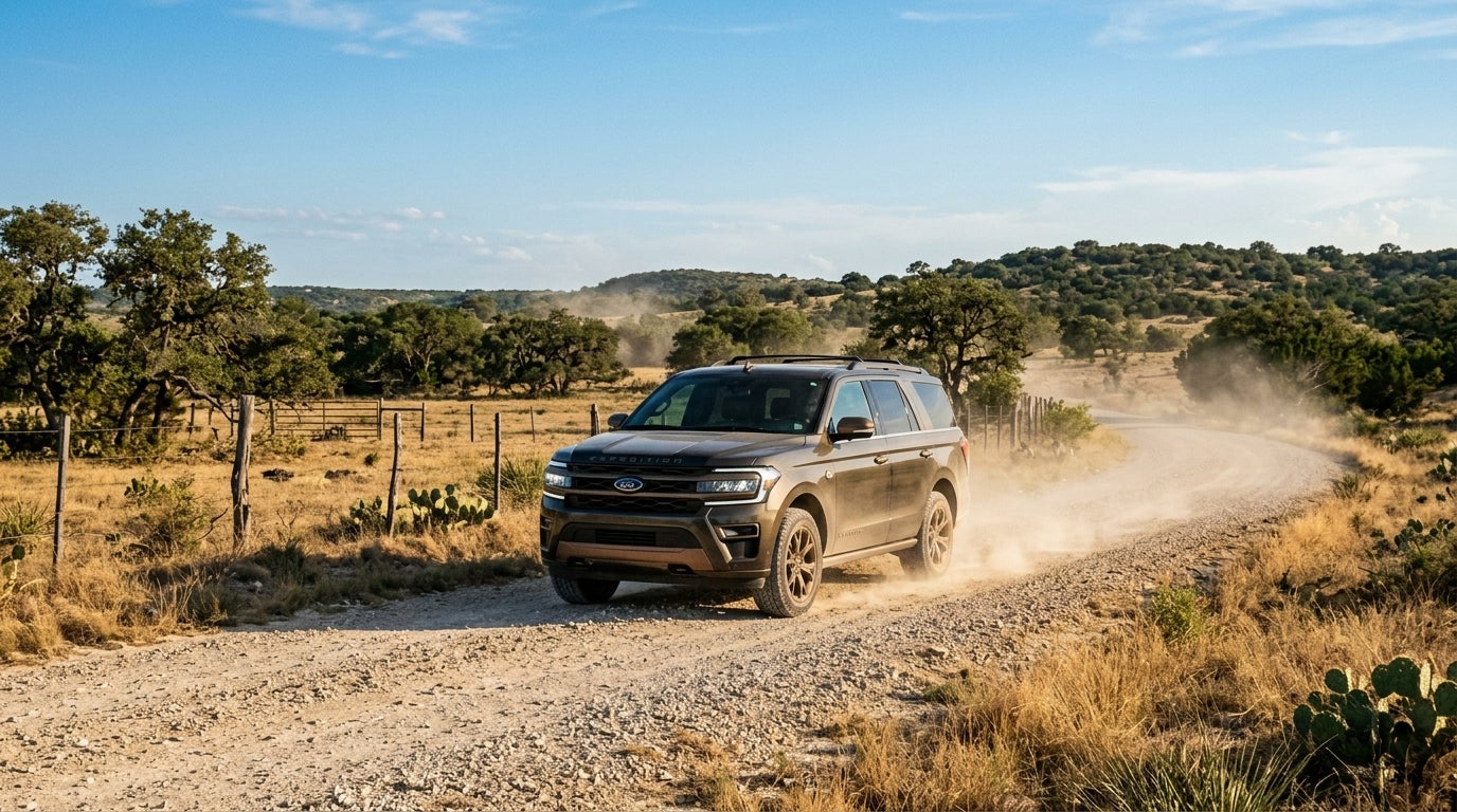 A bronze Ford Expedition driving on a dusty gravel road through a rural landscape.