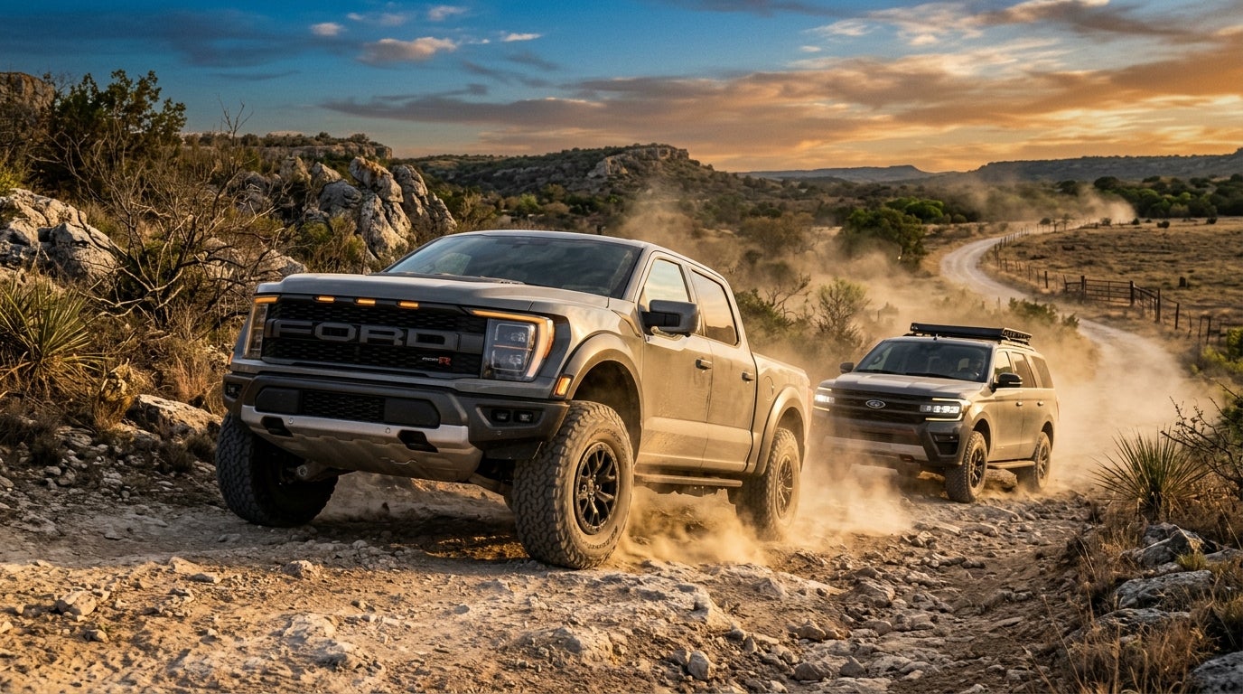 A gray Ford F-150 Raptor R and a gray Ford Expedition driving off-road on a rocky trail at sunset.