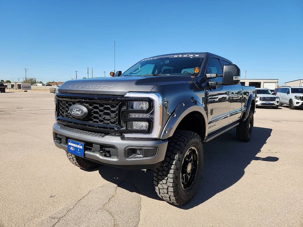 Lifted Ford Super Duty pickup truck with custom off road tires and black grille parked outdoors under clear blue sky