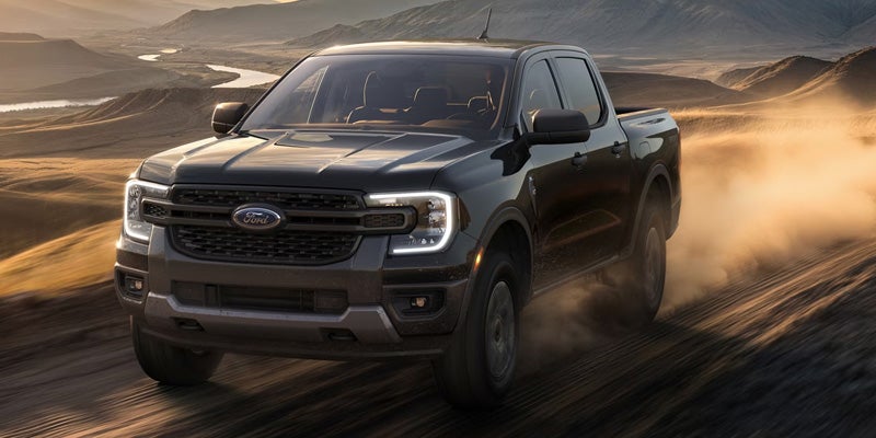 a black 2026 Ford Ranger truck drives through a dusty, sandy region