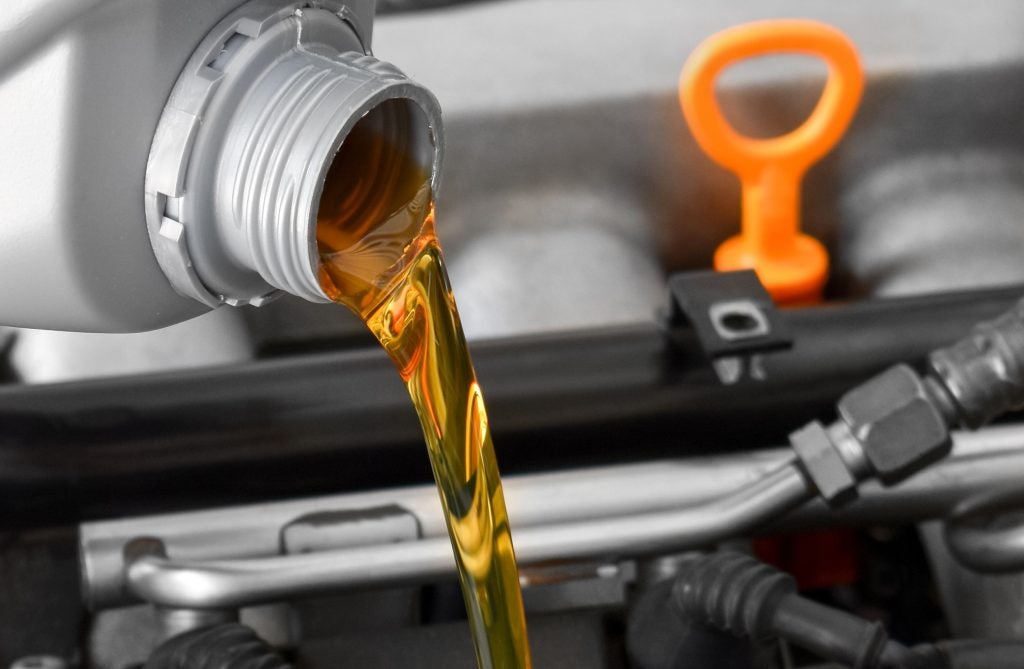 Engine oil being poured into a car engine with dipstick visible in the background.