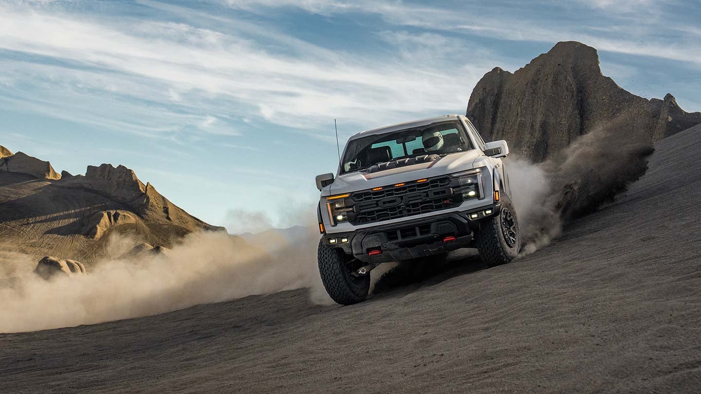 A 2026 Ford F-150 driving through a sandy desert landscape, showcasing its rugged design and off-road capabilities.