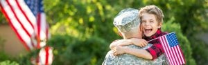Child hugging a military service member while holding an American flag