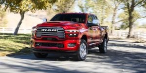 Red RAM truck driving down a tree-lined road with a scenic background.