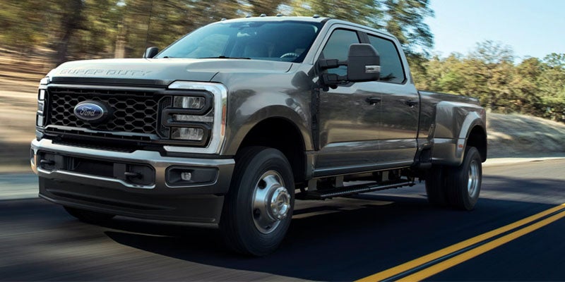 A gray Ford pickup truck driving on a road surrounded by trees.