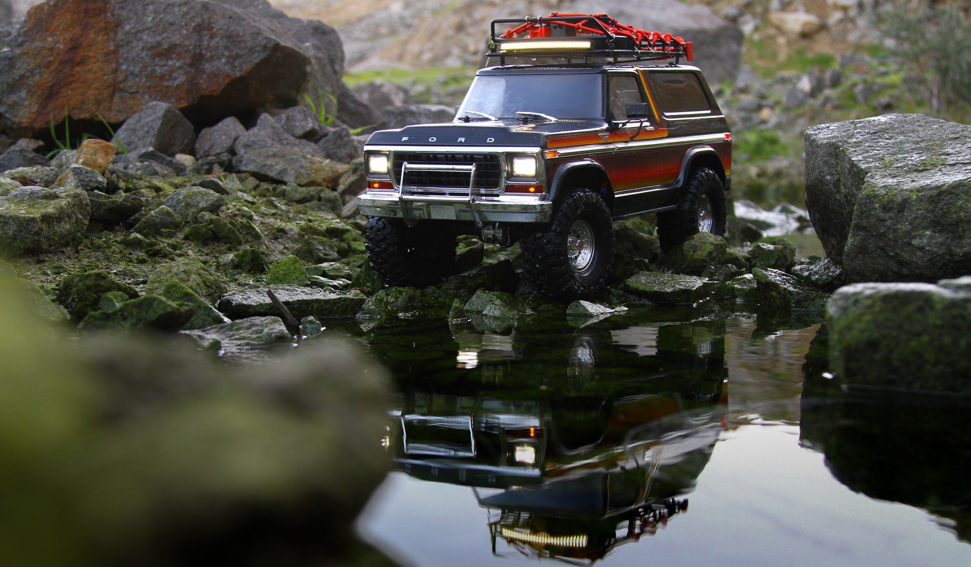 An off-road, rugged Bronco mid-size SUV driving on rocks near water