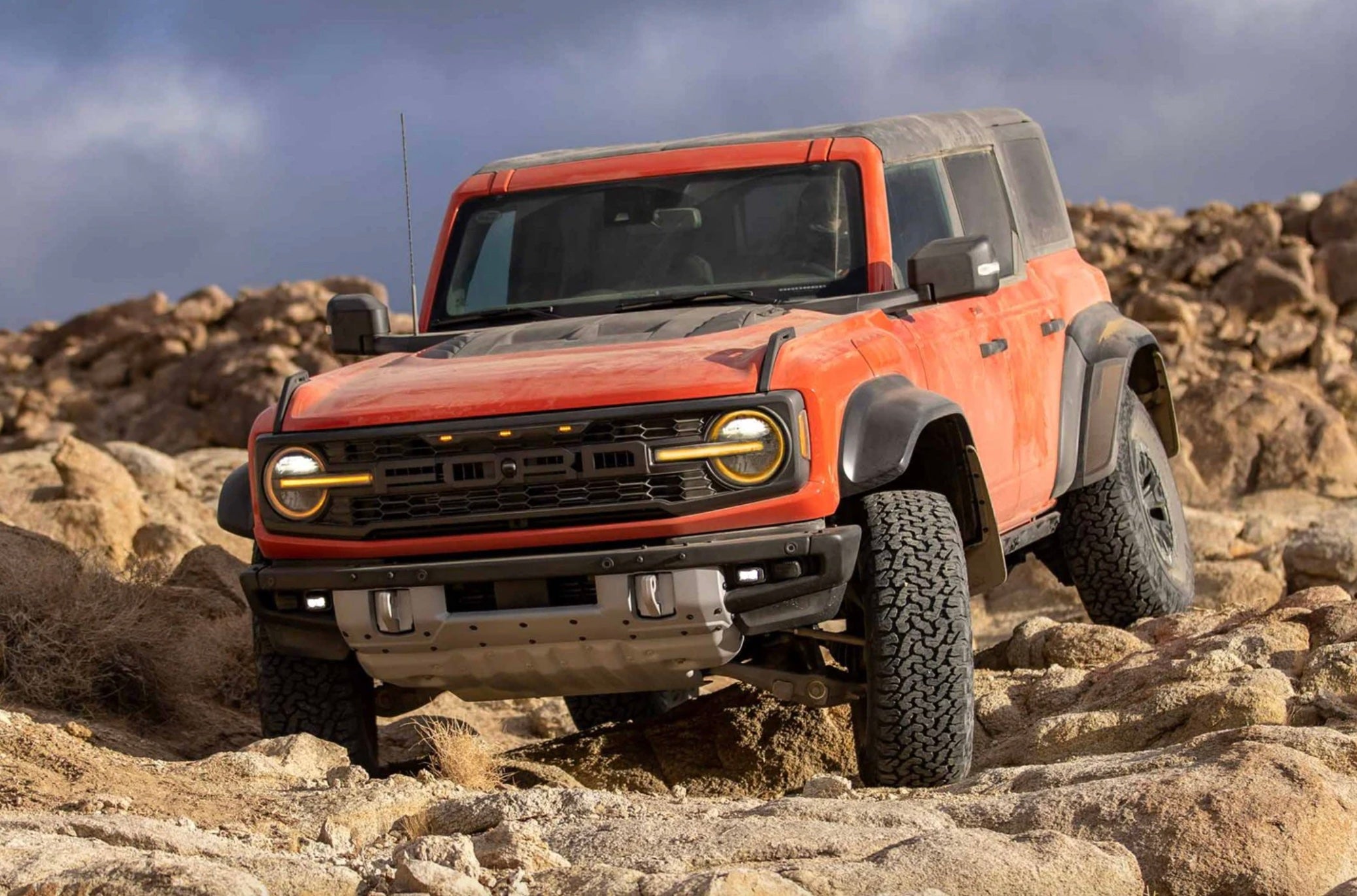An orange 2022 Ford Bronco Raptor SUV off-roading on rocky terrain.