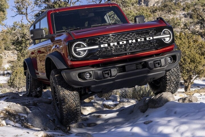 A red Ford Bronco SUV driving on rough terrain.