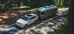 White Jeep Grand Cherokee pulling a trailer bus behind it on a neighborhood road.