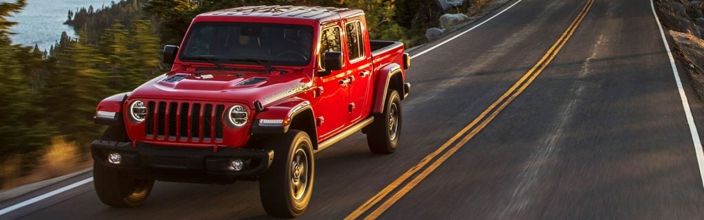 Bright red Jeep Gladiator pickup truck driving on a paved road