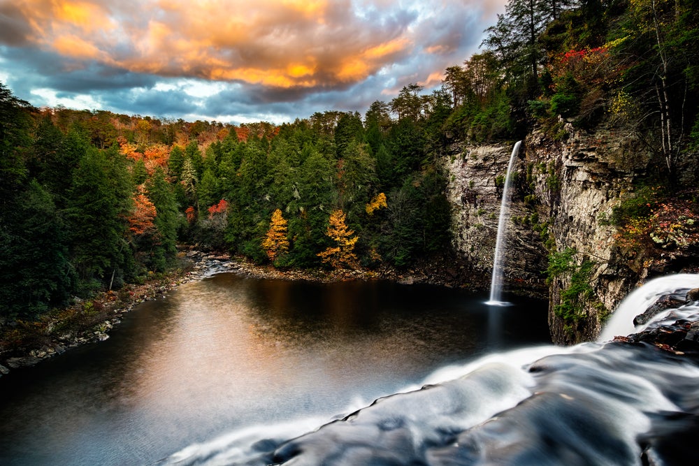 Tennessee state park view from the top of a waterfall overlooking a water reservoir with fall colored leaves and a tall, skinny waterfall to the left.