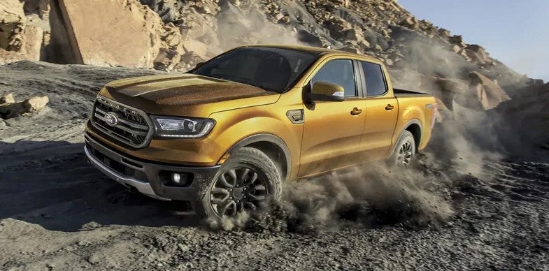 New yellow gold 2022 Ford Ranger driving off road in rocky mountainous terrain.