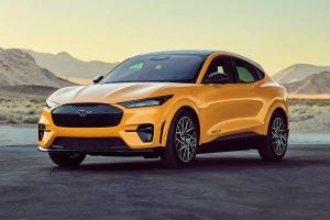 Gold colored Ford Mustang Mach E angled left in front of a desert backdrop