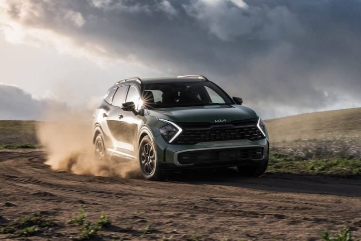 2025 Kia Sportage kicking up dirt as it drives off-road in a rugged landscape.