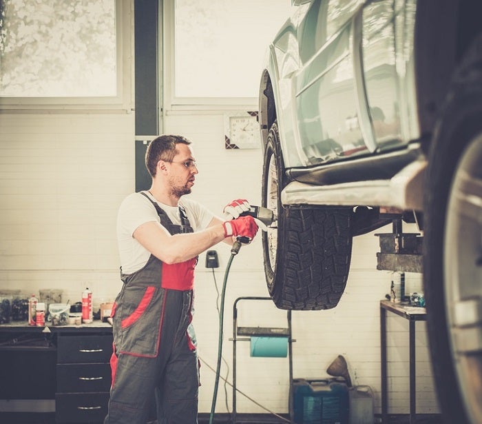 Serviceman unscrewing wheel in car workshop