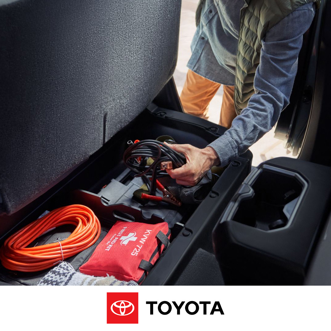 A person placing jumper cables into an under-seat storage compartment next to an orange rope and a first-aid kit.