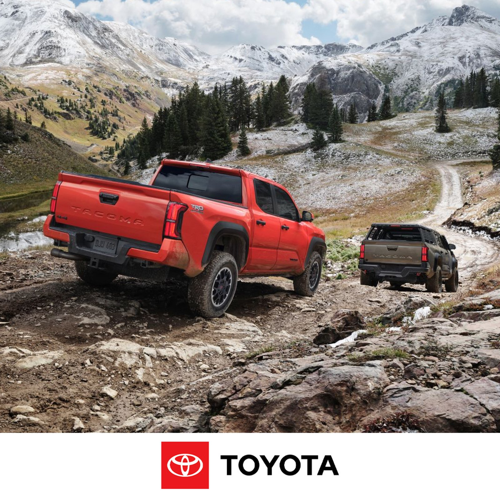 Rear view of a red Toyota Tacoma pickup truck with a bed rack, driving on a rocky dirt path.
