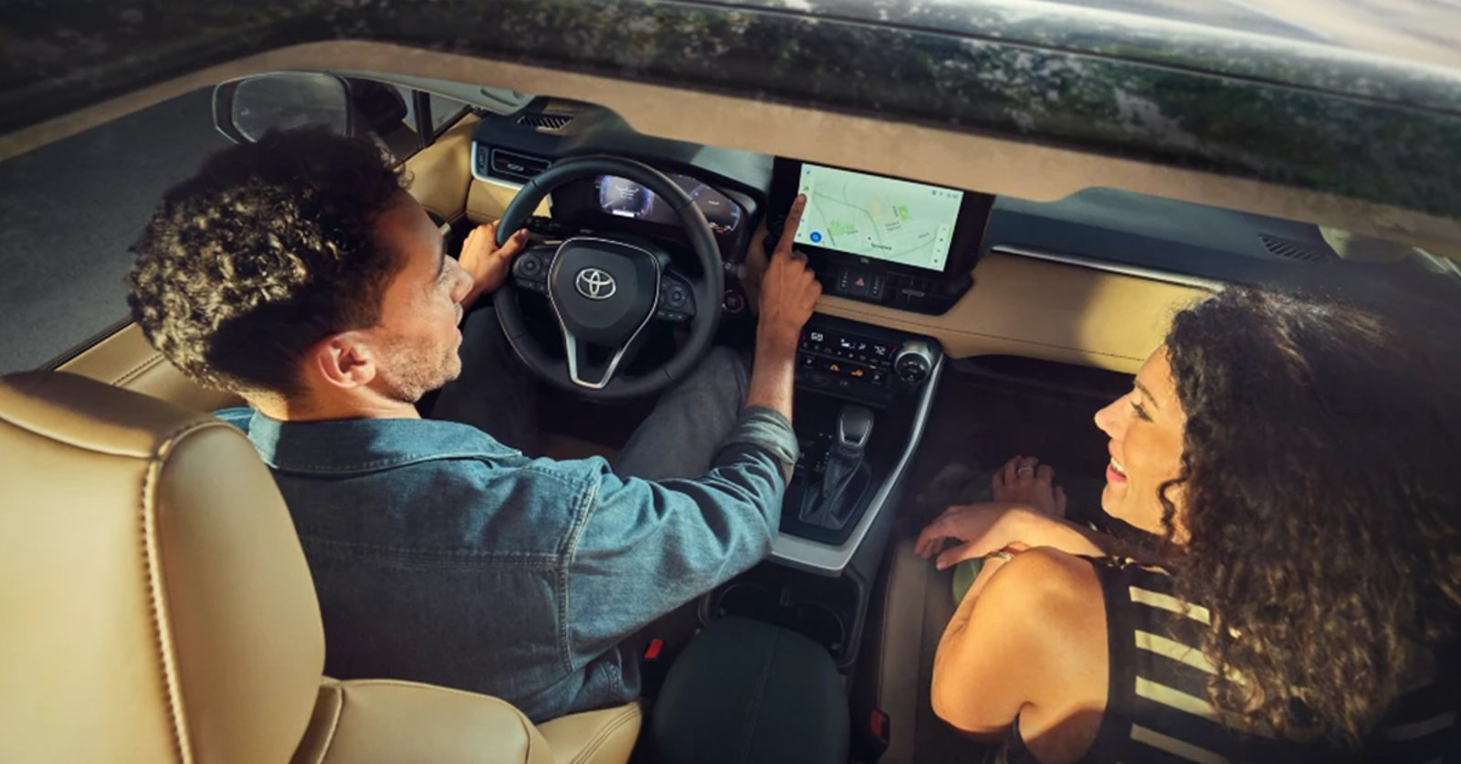 Man in a car, seen from the side, operating the center touchscreen display with his right hand.