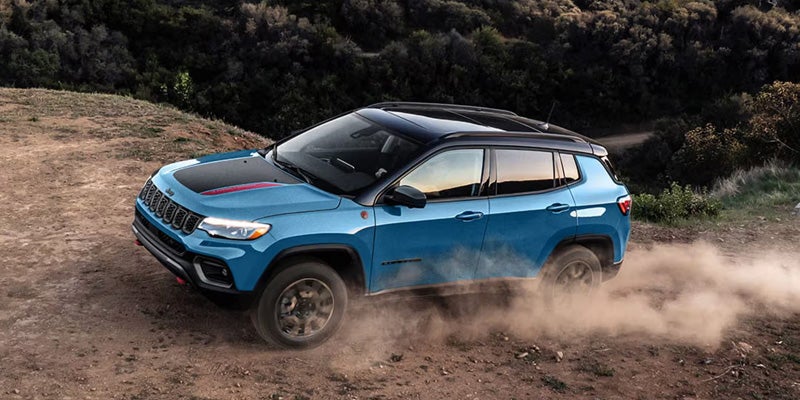 Blue Jeep SUV driving on a dirt trail with dust rising behind it.