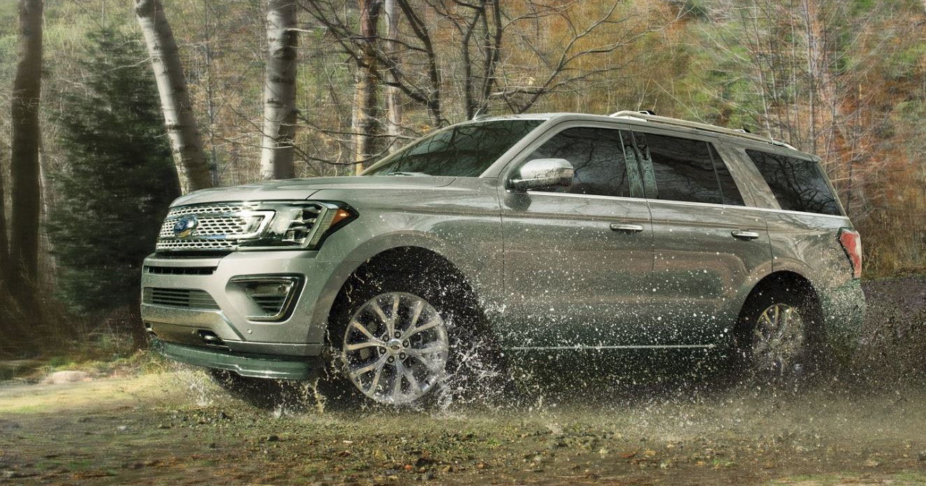 A silver 2019 Ford Expedition Titanium edition driving through a puddle in a forest.