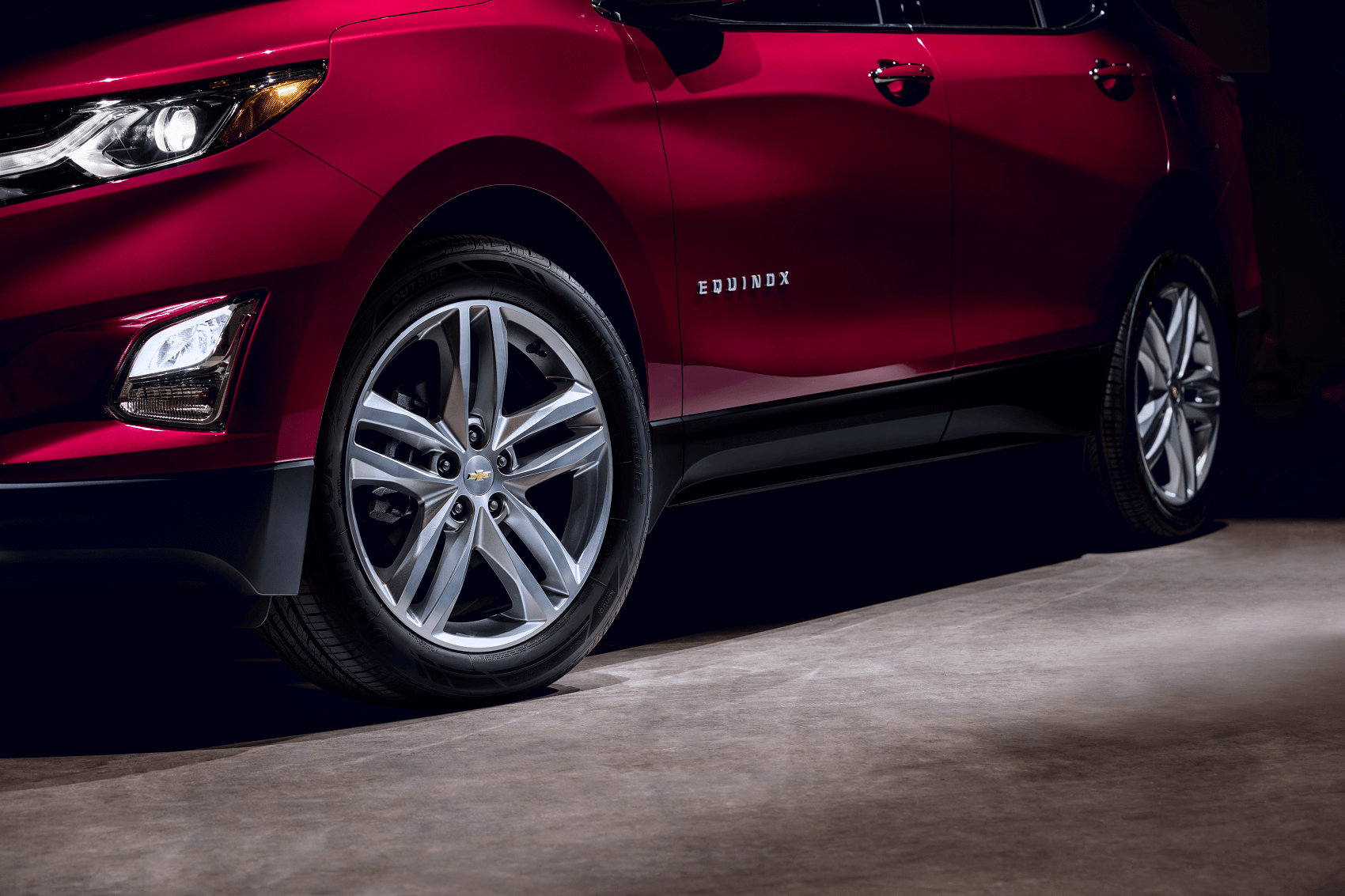 A shiny, red, brand-new Chevy Equinox is parked in a dramatically lit garage