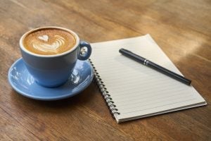 A coffee with heart are inside made with mike, next to a notebook and a pen