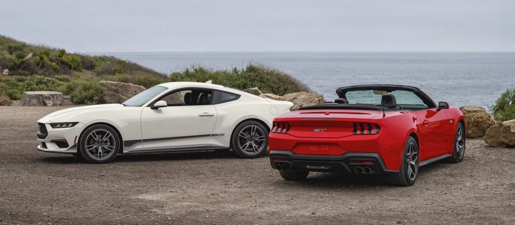 Two sports cars parked by the seaside road, highlighting sporty design and open-air driving experience.