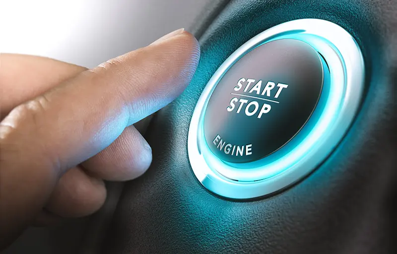 A finger pressing a car’s illuminated start/stop engine button.