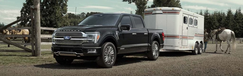 A pickup truck towing a horse trailer on a rural path, highlighting strong hauling capability.