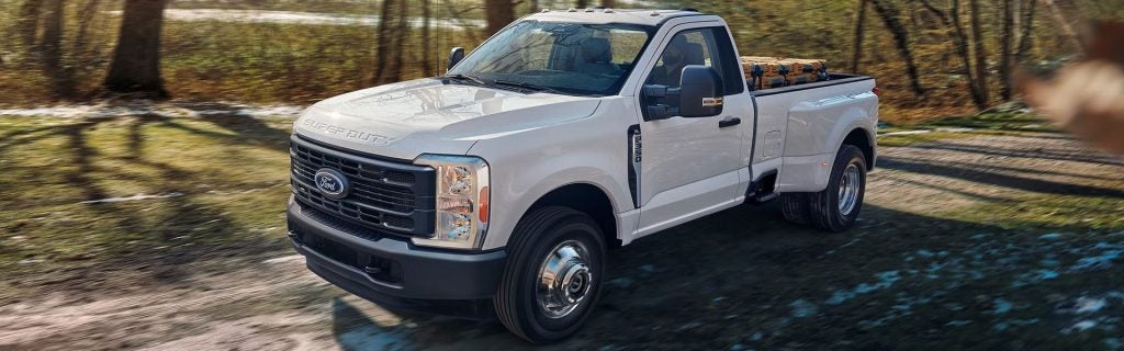 A white pickup truck driving on a dirt road, built for heavy-duty work and outdoor use.