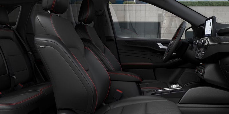 Modern car interior with black leather seats and red stitching.