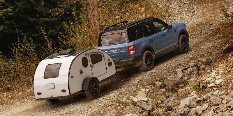 Blue SUV towing a small camper trailer on a rocky off-road path.