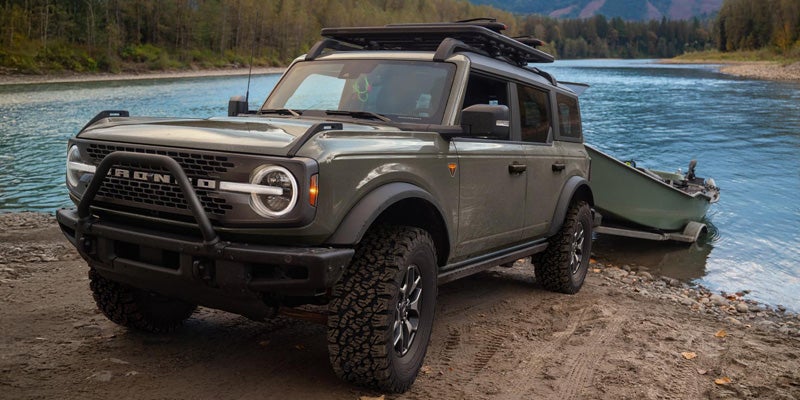 A rugged off-road SUV parked by a riverside, towing a small boat and ready for outdoor adventure.