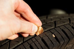 A hand holding a penny into a tire tread - A quick an easy test to asses the need for tire care