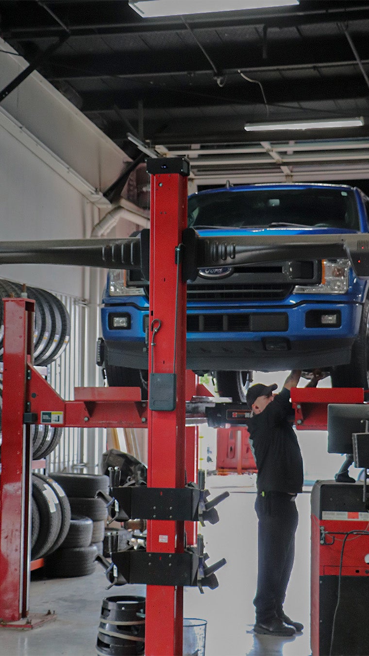 A technician working beneath a blue Ford F-150 on a lift at Atchinson Ford