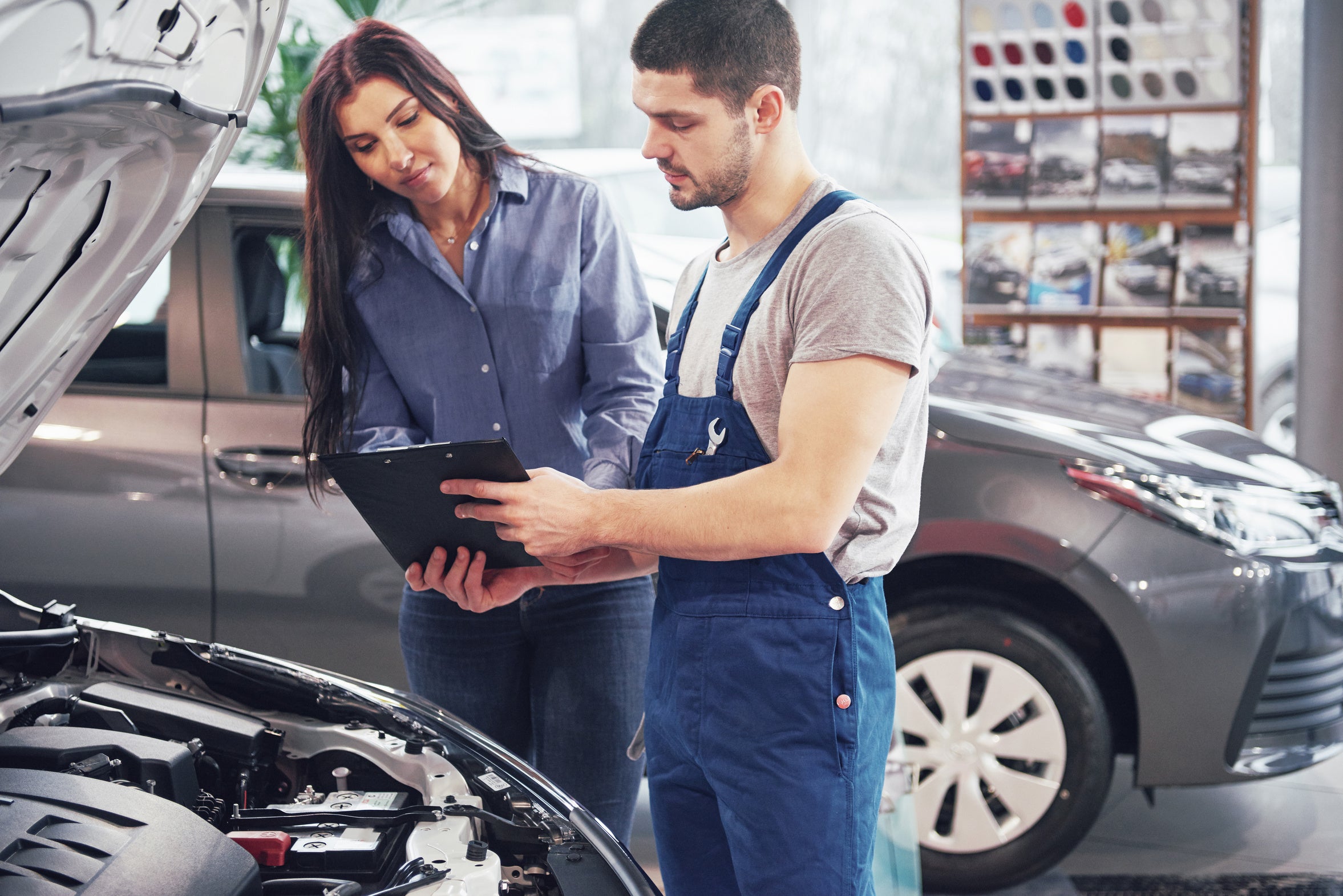 A mechanic and customer reviewing information beside an open vehicle hood