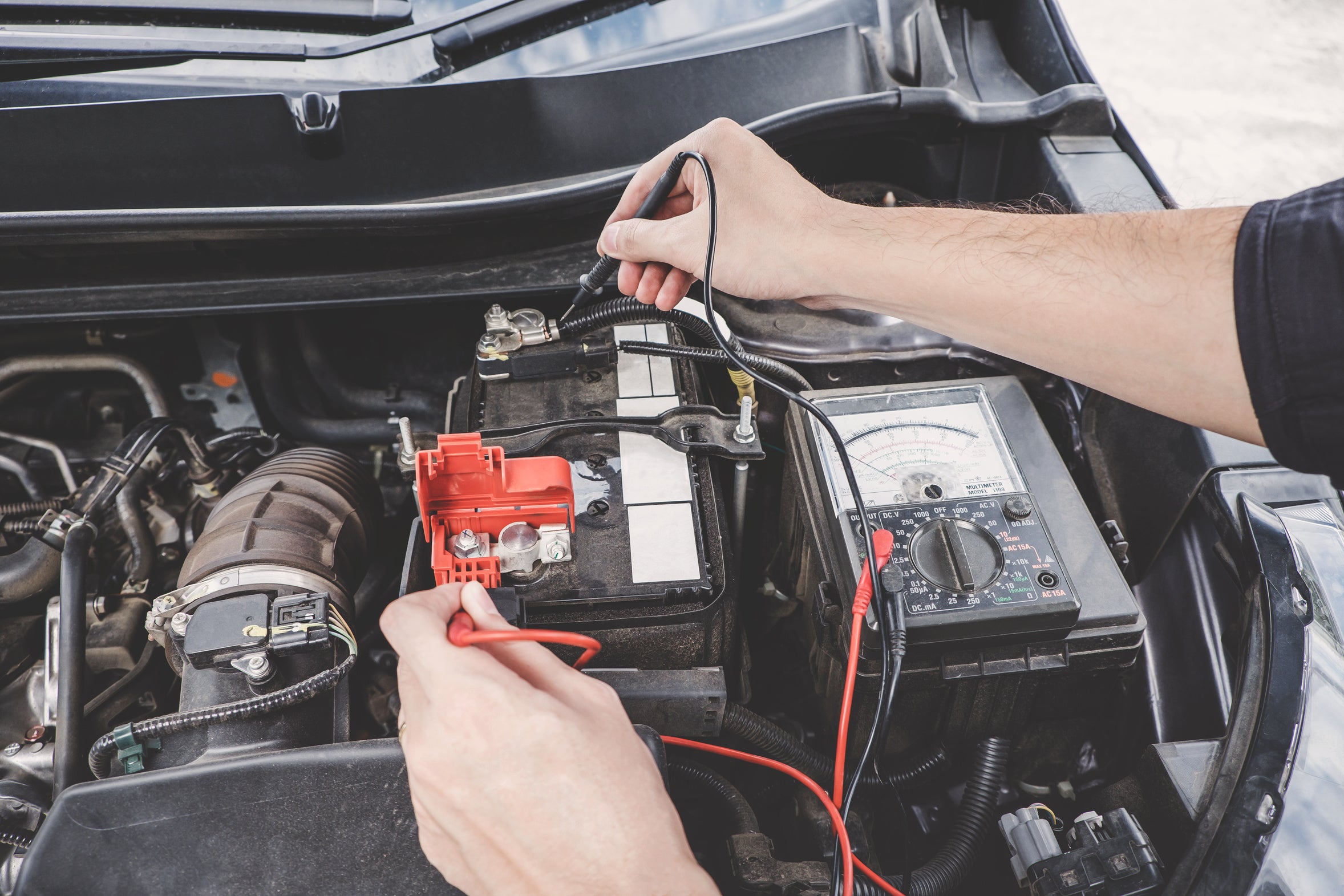 A technician testing a vehicle battery with a digital meter