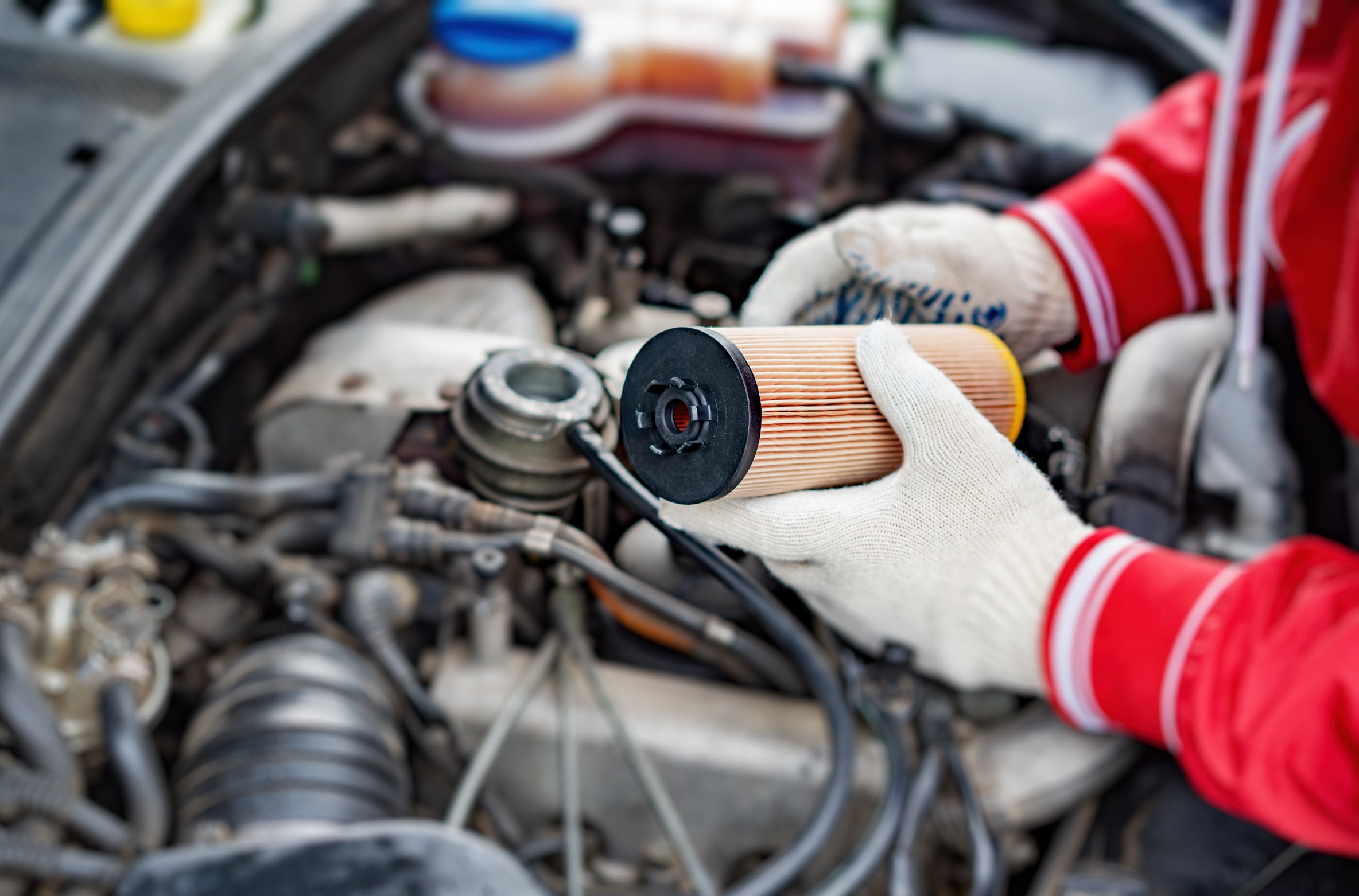 A technician holding an oil filter above an engine compartment