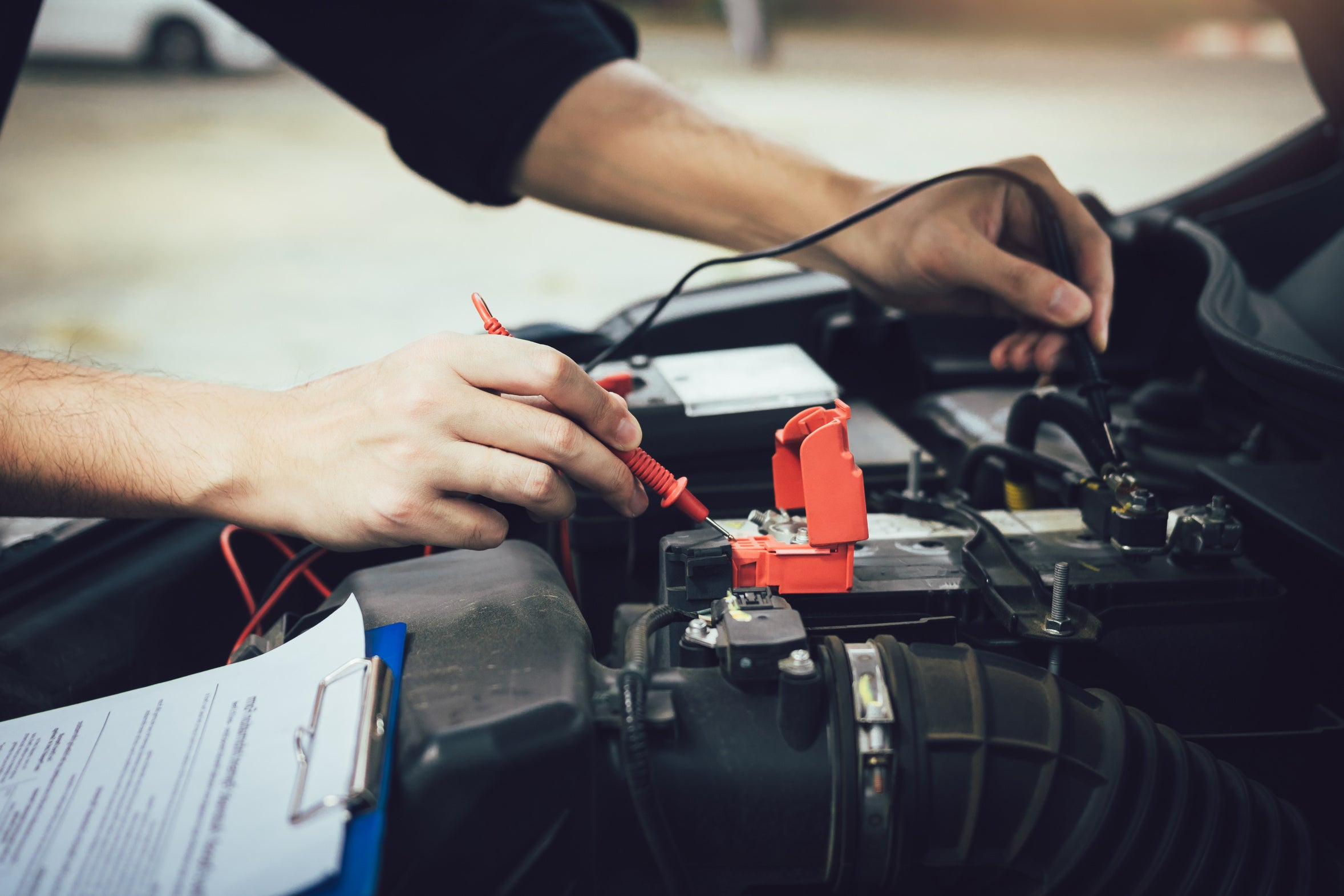 A technician connecting a battery test instrument in an engine compartment