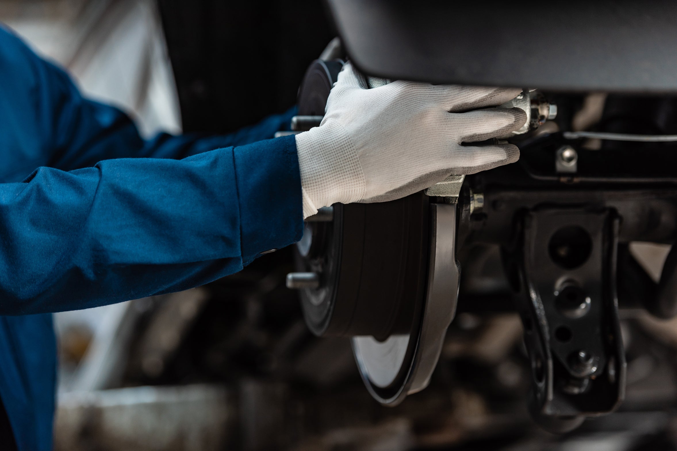 Gloved hands inspecting an exposed brake disc and caliper