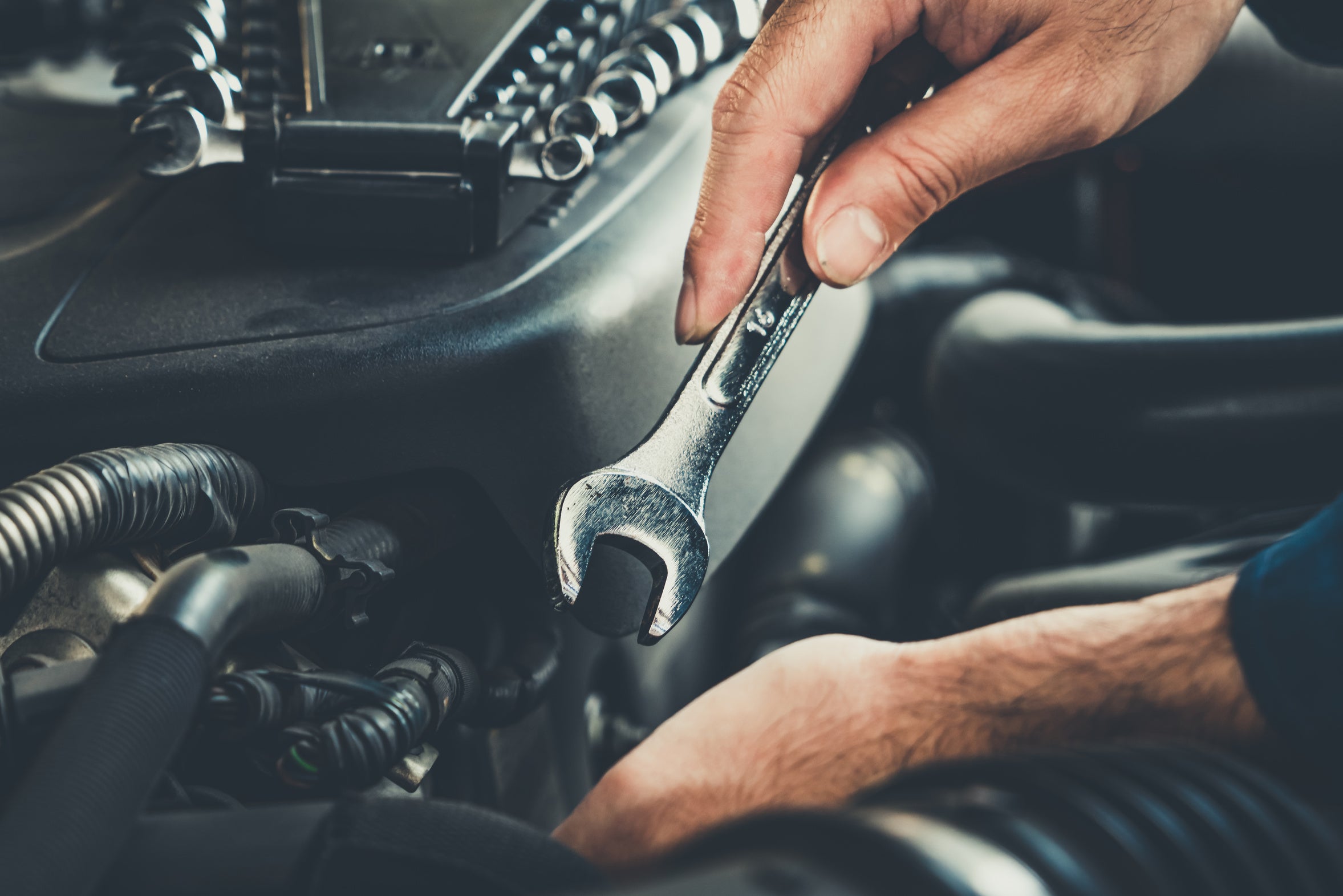 Hands using a wrench to work on a vehicle engine
