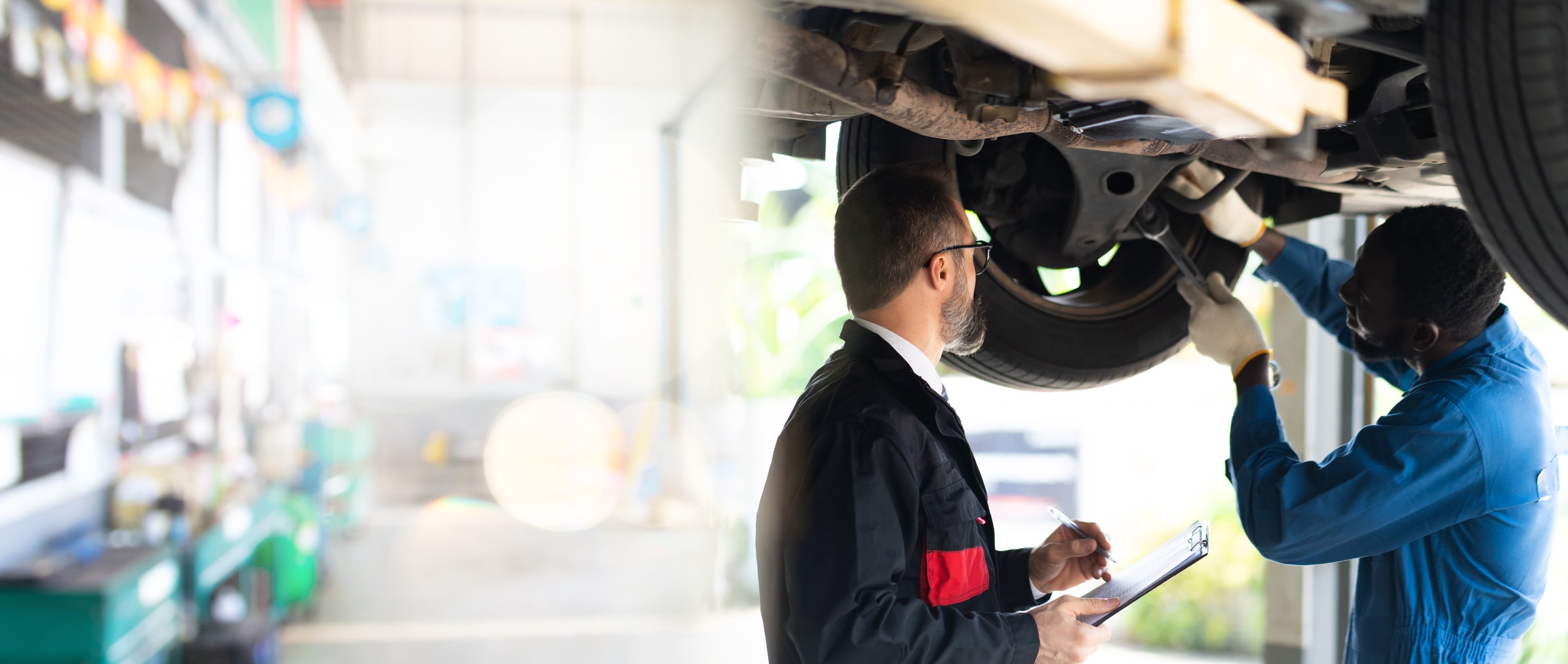 Two workshop professionals discussing work beneath a raised vehicle