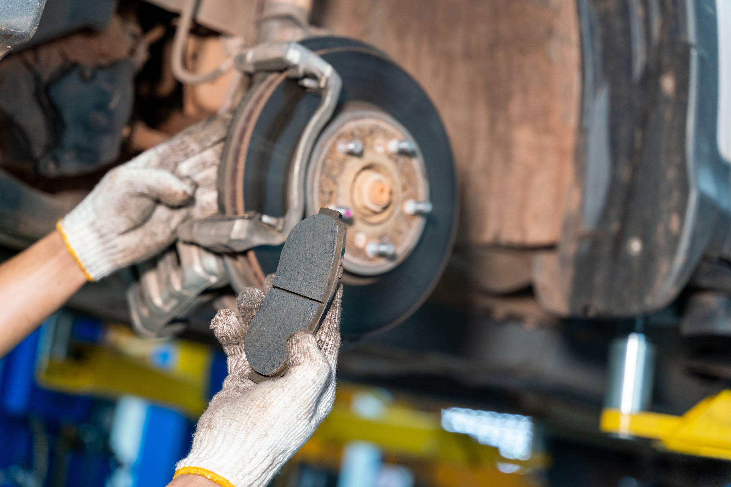 A technician inspecting a vehicle brake pad and exposed brake assembly
