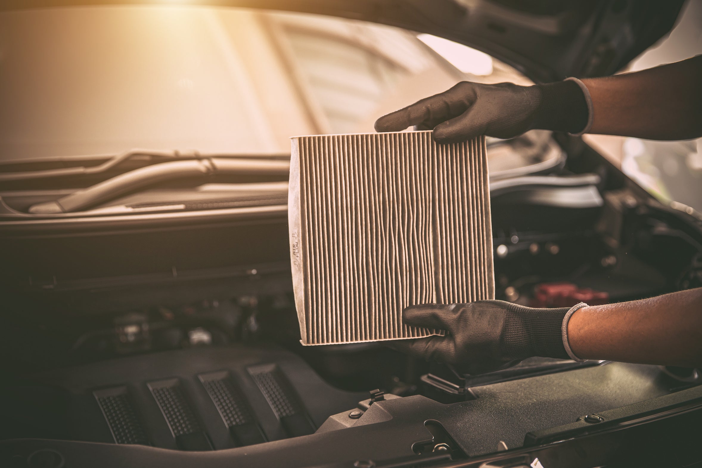 Hands inspecting a vehicle air filter above an open engine bay