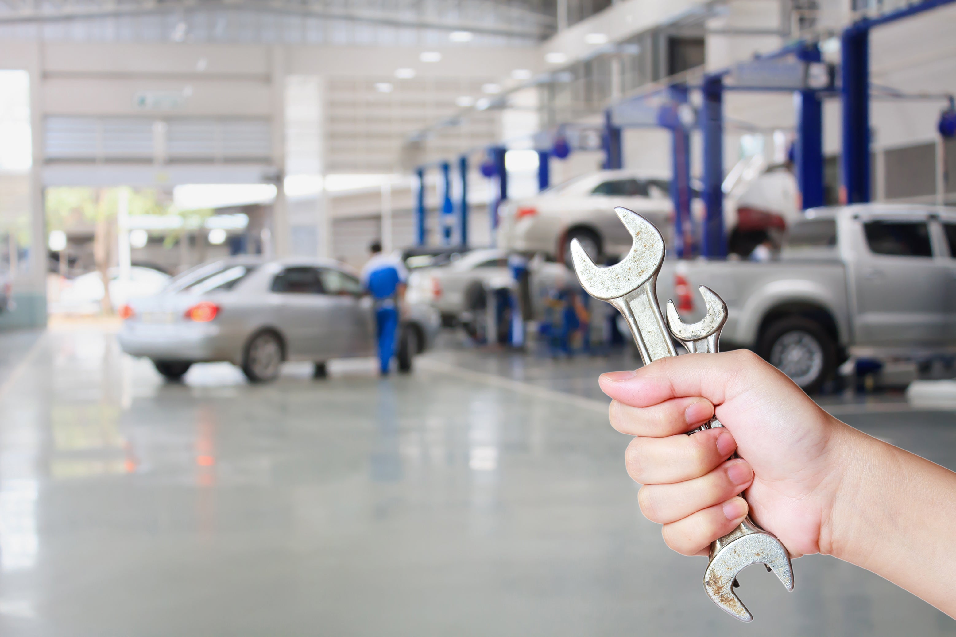 A hand holding a workshop wrench with a service bay in the background