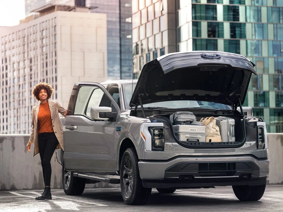 Woman loading gear into the open F-150 Lightning Mega Power Frunk on a city street